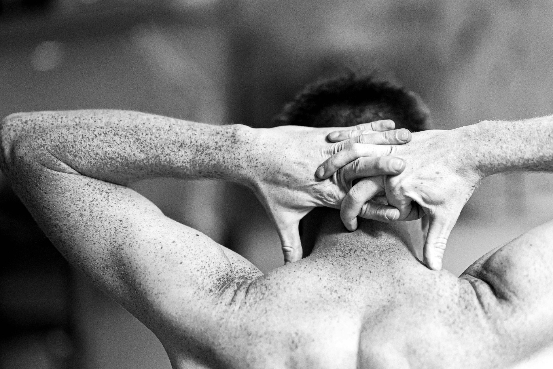 Black-and-white photograph of a man's back and shoulders, hands clasped behind his head