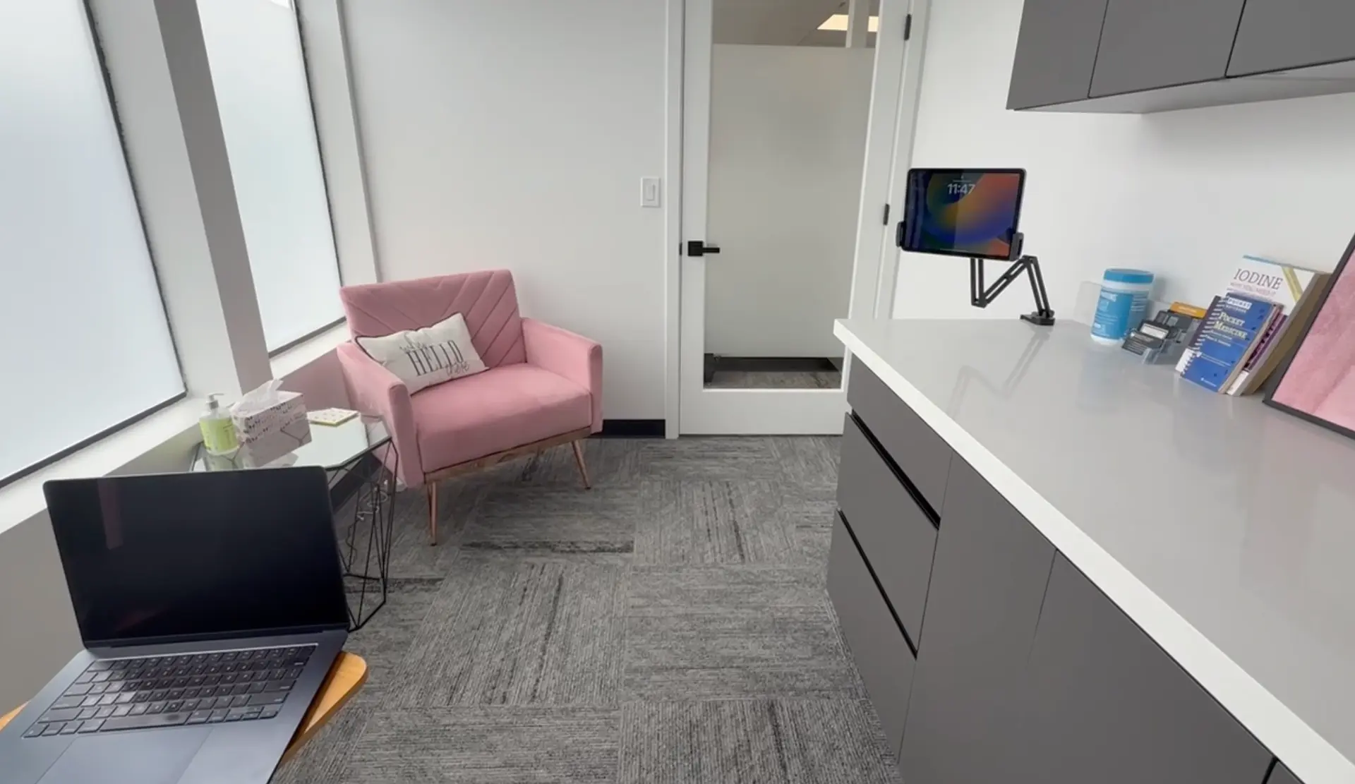 Consultation room with a pink armchair, laptop workstation, and medical reference books