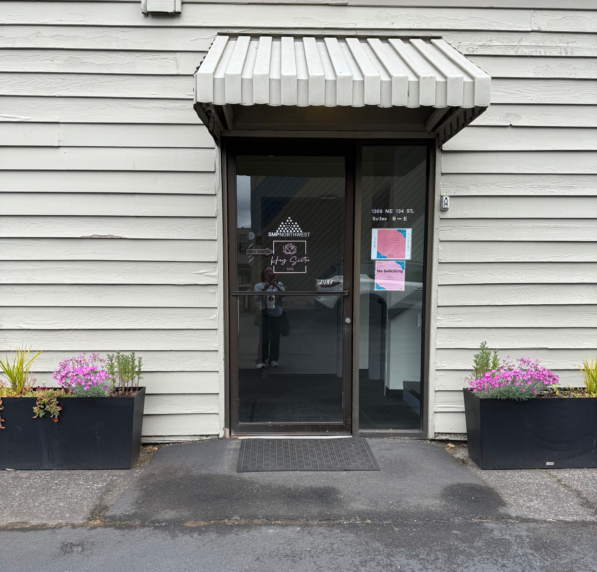 Front entrance of the Storm Wellness Northwest office, with the glass door behind the white awning and planters on either side