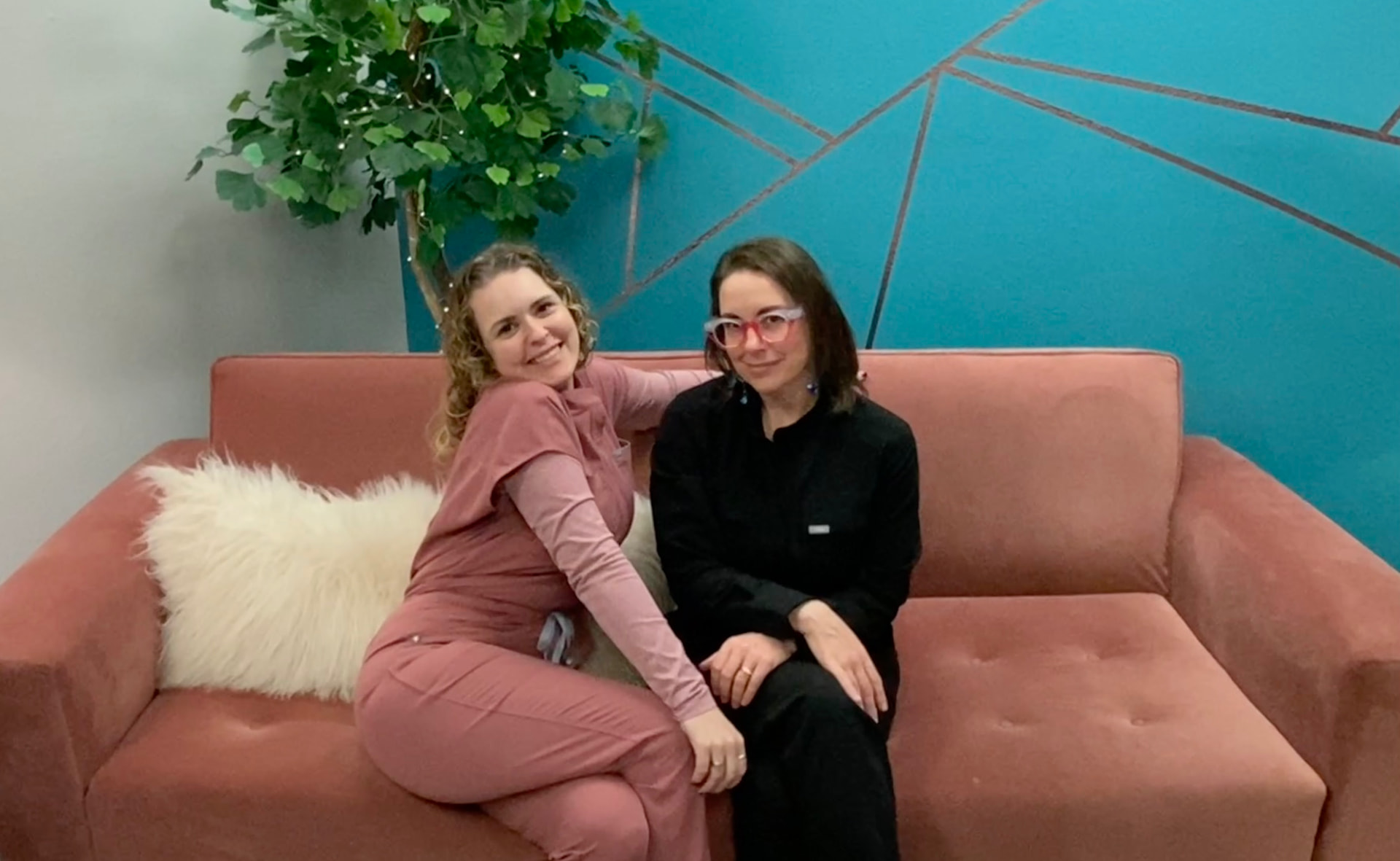 Renee Storm and her sister sitting together on the pink couch in their first office