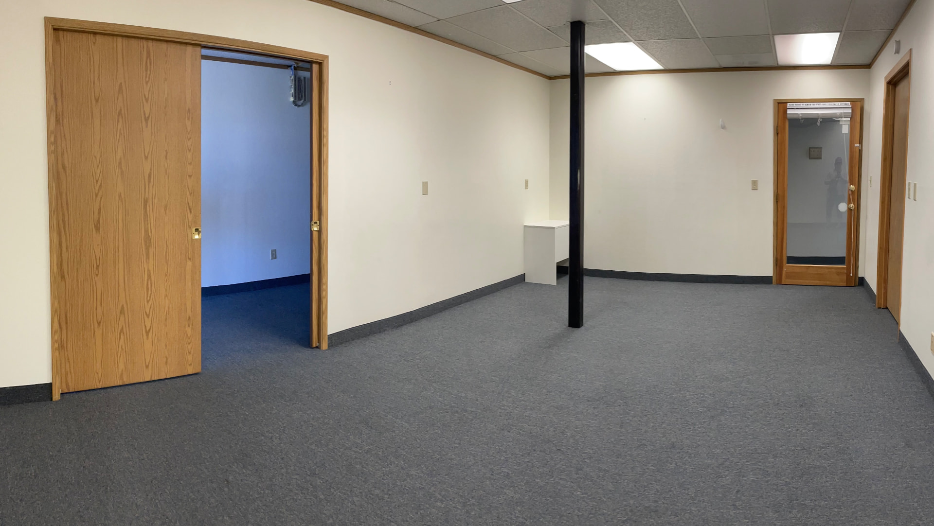 Empty office room with wood doors, support post, and grey carpet before renovation